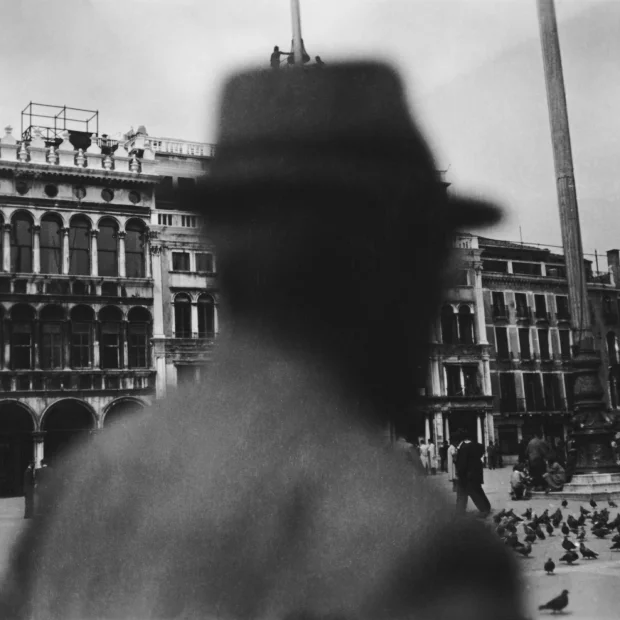 Man in hat, standing in front of a building.